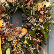 Close-up of the Spiced Clementine Luxury Winter Wreath showcasing dried clementines, golden berries, and rustic accents like thistle and bracken.