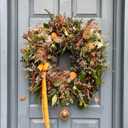 Spiced Clementine Winter Wreath hanging on a door, showcasing lush greenery, dried clementines, and festive natural touches.